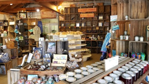 A cozy market display featuring wooden crates, jars, baked goods, and various local products for sale.