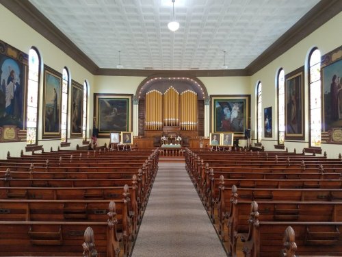 Interior of a church featuring wooden pews, large stained glass windows, and an ornate organ at the front.