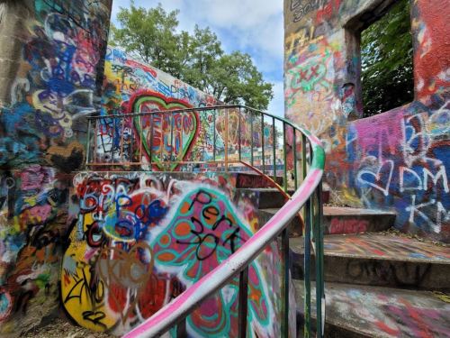 A spiral staircase surrounded by colorful graffiti on stone walls and greenery above.