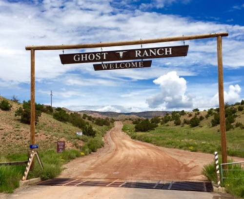 A wooden sign reading "Welcome to Ghost Ranch" over a dirt road, surrounded by green hills and blue skies.