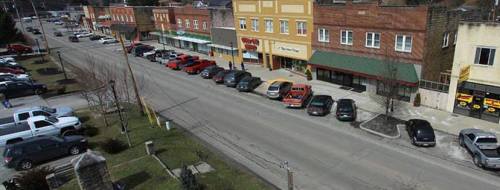 A view of a small town street lined with parked cars and storefronts on either side, under a clear sky.