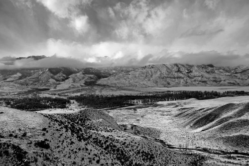 A dramatic black and white landscape featuring mountains, valleys, and clouds, creating a moody, atmospheric scene.