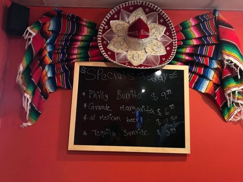 A chalkboard menu displaying daily specials at a Mexican restaurant, surrounded by colorful sombreros and blankets.