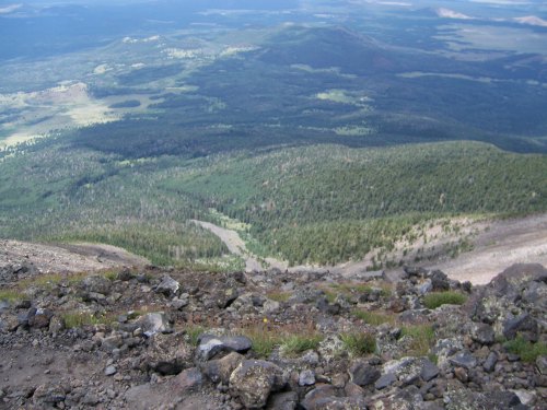 A panoramic view from a mountain summit, showcasing lush green valleys and rocky terrain below.