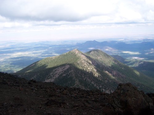 A panoramic view of green mountains under a cloudy sky, with shadows cast on the landscape below.