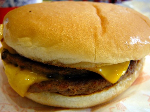 Close-up of a cheeseburger with two beef patties and melted cheddar cheese, served in a soft bun.