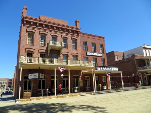 Historic brick buildings in a western-style town, featuring balconies and storefronts under a clear blue sky.
