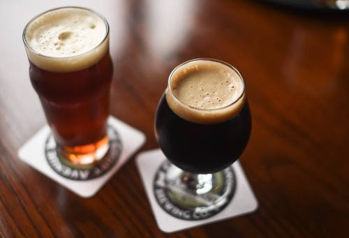 Two glasses of beer on coasters: one amber ale in a tall glass and one dark stout in a short, round glass.
