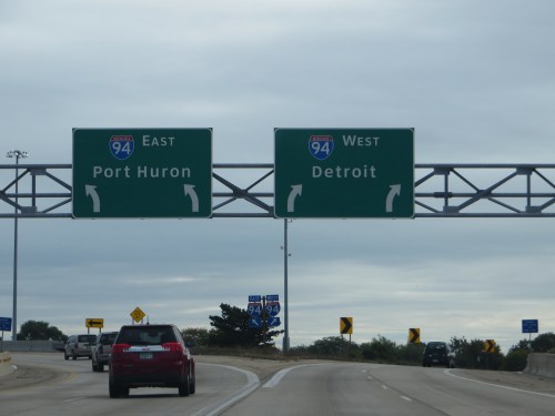 Highway sign indicating I-94 East to Port Huron and I-94 West to Detroit, with cars approaching the interchange.