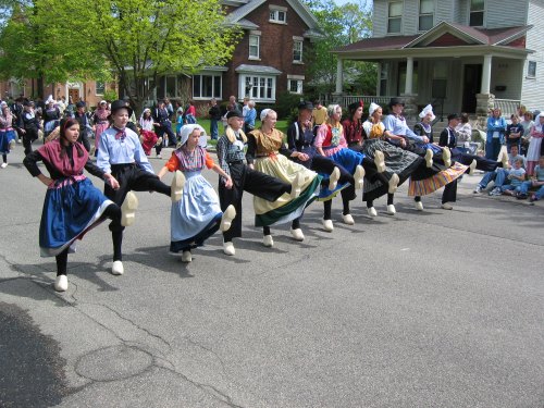A group of dancers in traditional costumes performing a lively dance on a street during a festival.