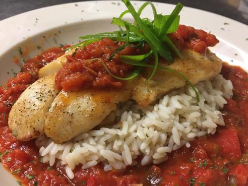 A plate of fish topped with tomato sauce, served over a bed of white rice and garnished with green onions.
