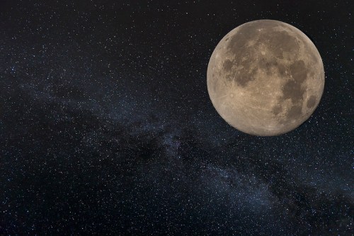 A bright full moon against a starry night sky, with a faint galaxy visible in the background.