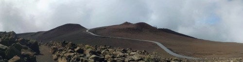 A panoramic view of a volcanic landscape with a winding road and rocky terrain under a cloudy sky.