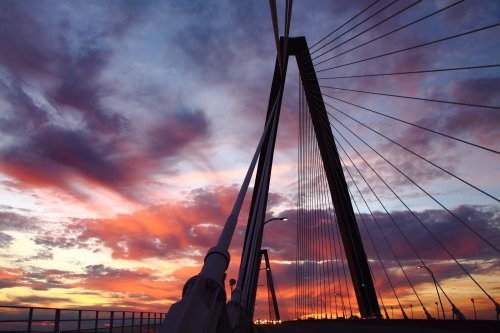 A silhouette of a cable-stayed bridge against a vibrant sunset with colorful clouds.
