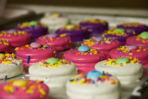 Colorful cookies with pink and white icing, topped with sprinkles and candy, arranged on a baking sheet.