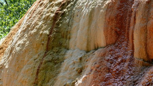 Close-up of a textured rock surface displaying various earthy colors and mineral deposits in natural sunlight.