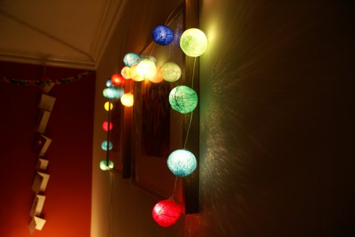Colorful string lights in various shades illuminate a wall, casting soft shadows and creating a cozy atmosphere.