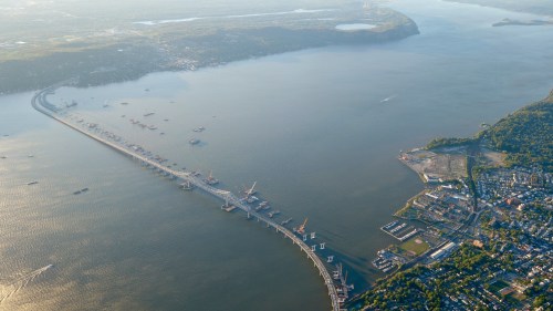 Aerial view of a long pier extending into a river, surrounded by boats and a town along the shoreline.