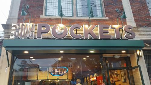 Sign for "East Side Pockets" with an illuminated "OPEN" sign, showcasing a brick building exterior.