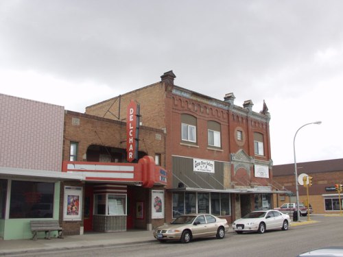 Historic buildings line a street, featuring the Delchar Theater with a marquee, under a cloudy sky.