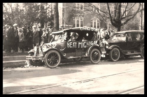 A vintage car decorated with "Beat Michigan" parked near a crowd, showcasing school spirit for Ohio State.