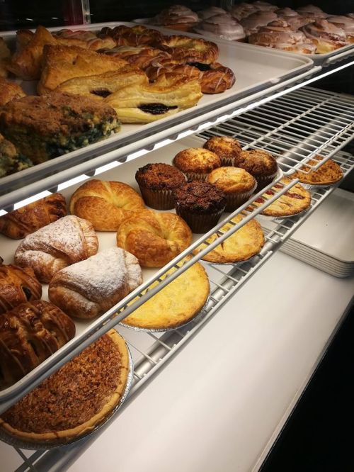 A display of assorted baked goods, including pastries, muffins, and tarts, arranged on shelves.