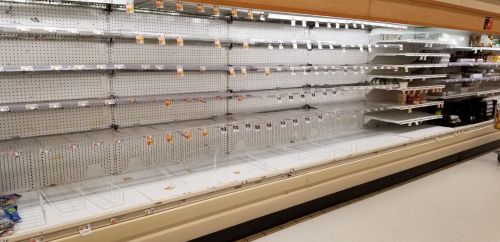 Empty grocery store shelves with minimal items, indicating low stock or high demand.