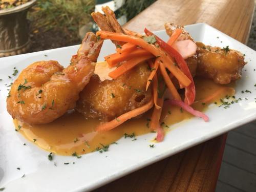 Three crispy shrimp topped with colorful vegetables, drizzled in a sweet sauce, served on a white plate.