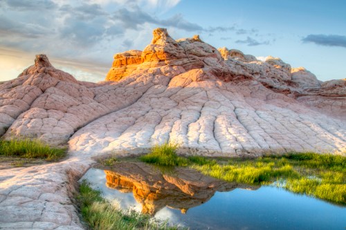 A serene landscape featuring textured rock formations and a calm pond reflecting the sky and surrounding greenery.