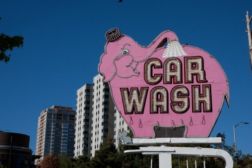 A large pink elephant-shaped sign for a car wash against a clear blue sky, with nearby buildings in the background.