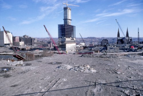 Construction site with cranes, a partially built tower, and a landscape of rubble against a clear blue sky.