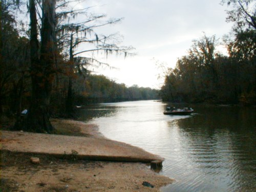 A serene river scene with a boat gliding through calm waters, surrounded by trees and autumn foliage.