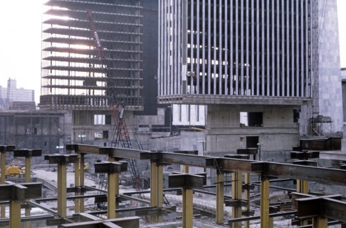Construction site featuring steel beams and two partially built skyscrapers against a city skyline.