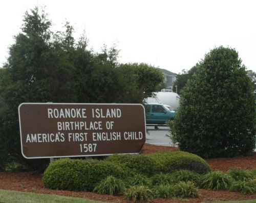 Sign for Roanoke Island, birthplace of America's first English child, 1587, surrounded by greenery.