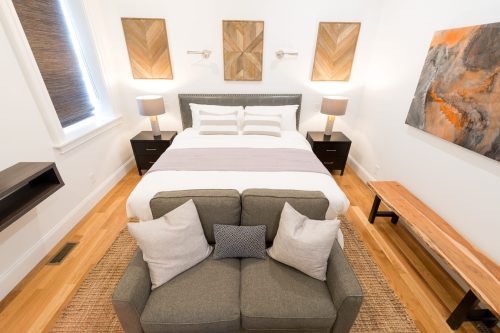 Cozy bedroom featuring a bed, two lamps, a sofa, and decorative wall art in a modern design.