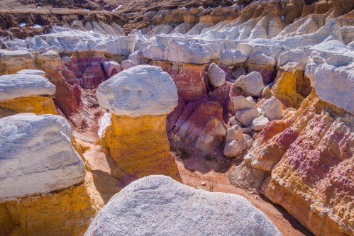 Colorful rock formations with layered textures in a canyon landscape, featuring white, yellow, and pink hues.