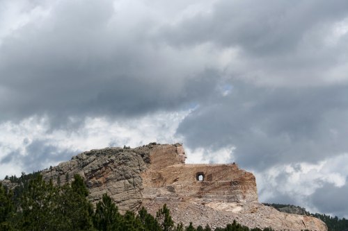 A rocky mountain landscape under a cloudy sky, featuring a distinct hole in the rock formation.