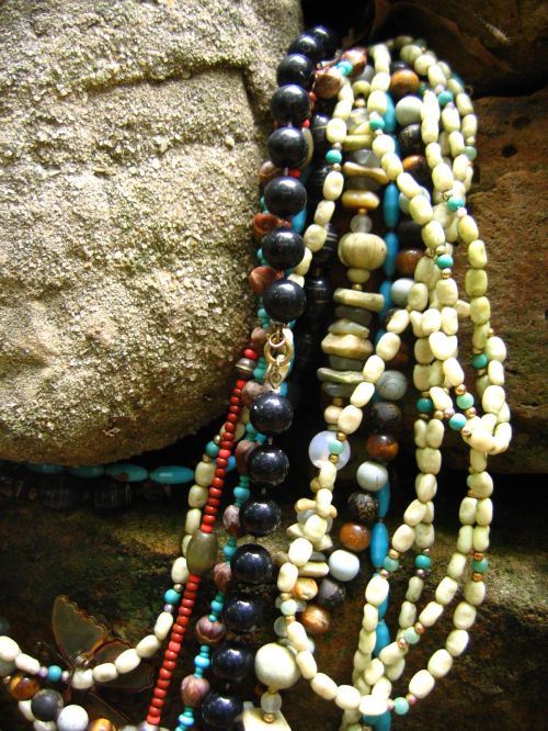 A close-up of colorful beaded necklaces draped over textured stones.