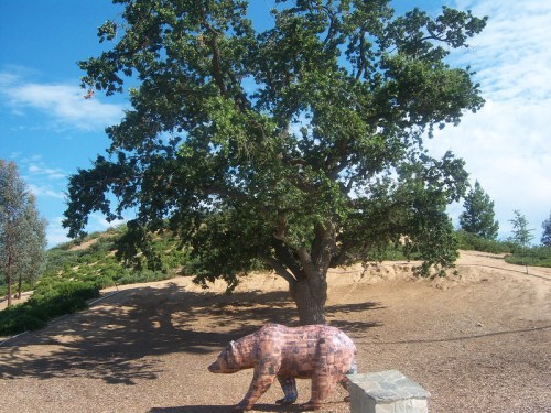 A large tree stands on a hillside with a bear sculpture made of bricks in the foreground.