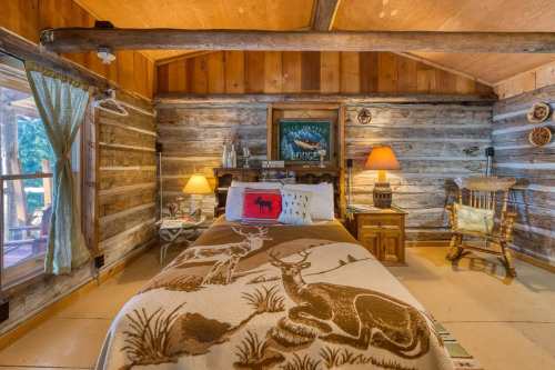 Cozy cabin interior with a wooden bed, rustic decor, and a rocking chair, featuring a warm color palette and natural light.