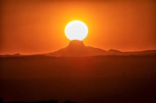 A large sun sets behind a mountain, casting a warm orange glow over the landscape.