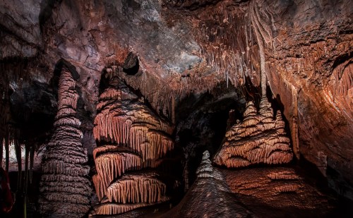 Stalactites and stalagmites in a dark cave, illuminated by warm light, showcasing intricate rock formations.
