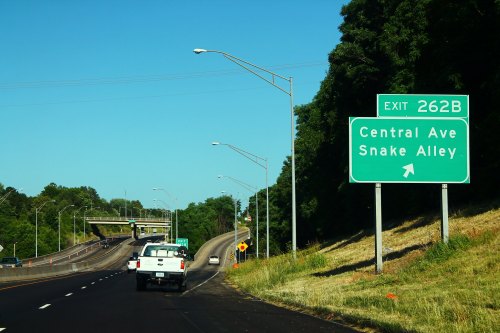 Highway exit sign for Central Ave and Snake Alley, with vehicles on the road and clear blue sky in the background.