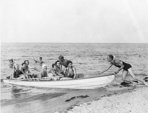 A group of people in swimsuits enjoying a day at the beach, some in a boat and others swimming in the water.