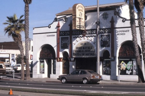 Historic building with a sign for John Mayall and the Youngbloods, featuring palm trees and a parked car in front.