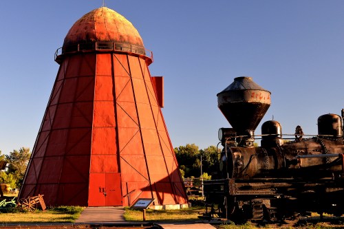 A red conical structure next to a vintage steam locomotive against a clear blue sky.