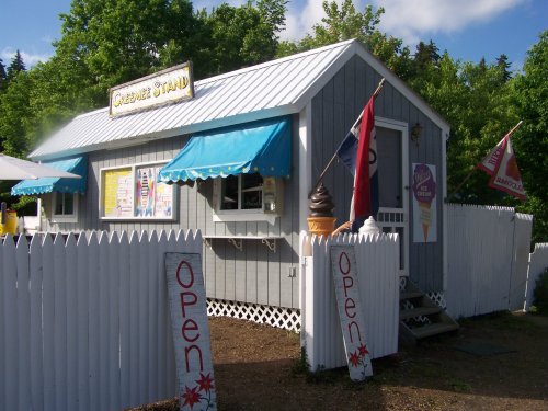 A charming ice cream stand with a white picket fence, blue awnings, and colorful flags, inviting customers inside.