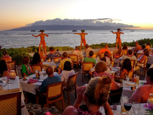 A sunset view of a restaurant with diners watching a traditional dance performance by two performers.