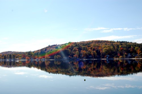 A serene lake reflects a colorful autumn landscape with trees and a clear blue sky.