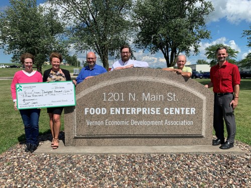 Group of six people holding a large check in front of the Food Enterprise Center sign on N. Main St. in Vernon.